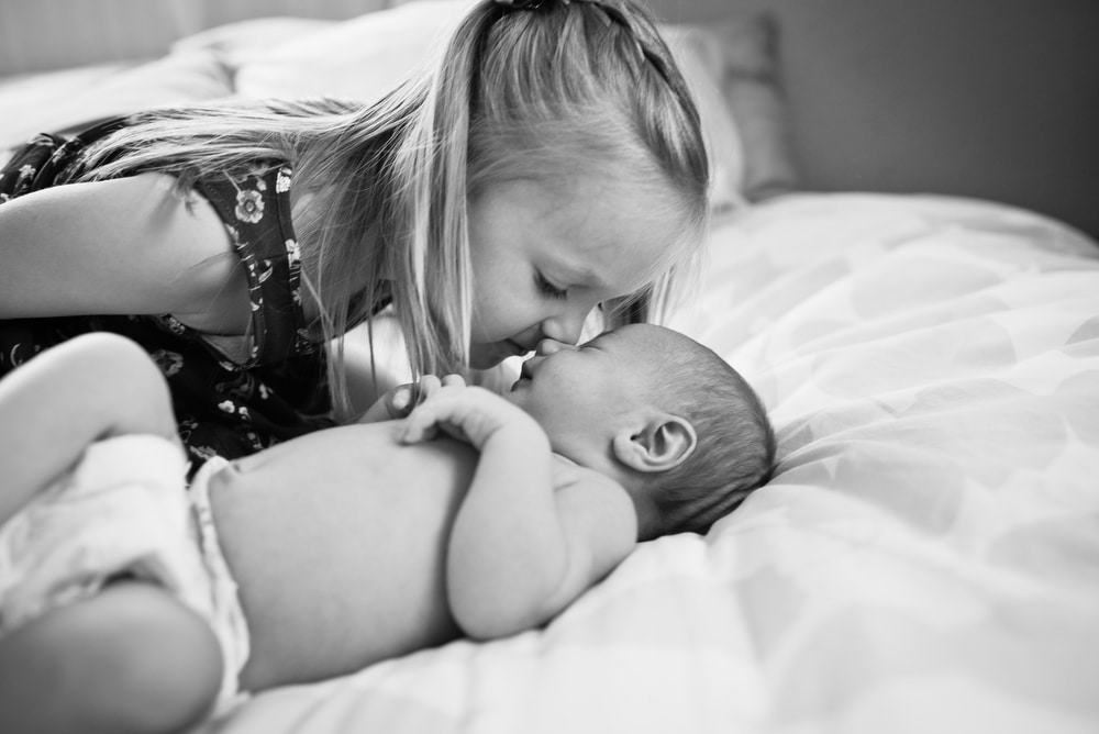 big sister kisses her newborn baby sister