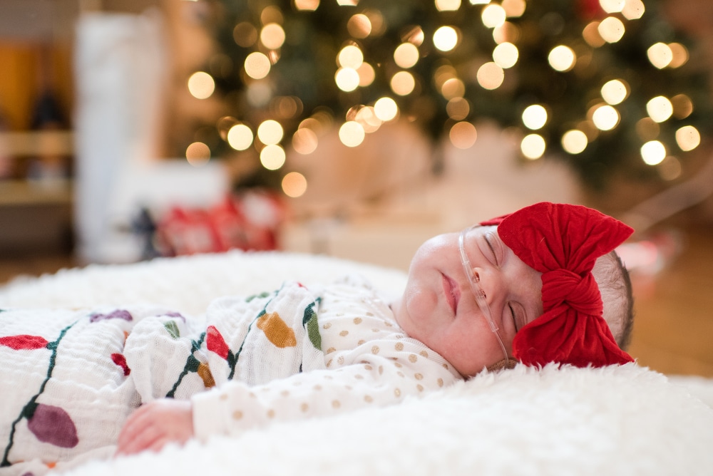 a preemie newborn lies in front of a Christmas tree during her portraits