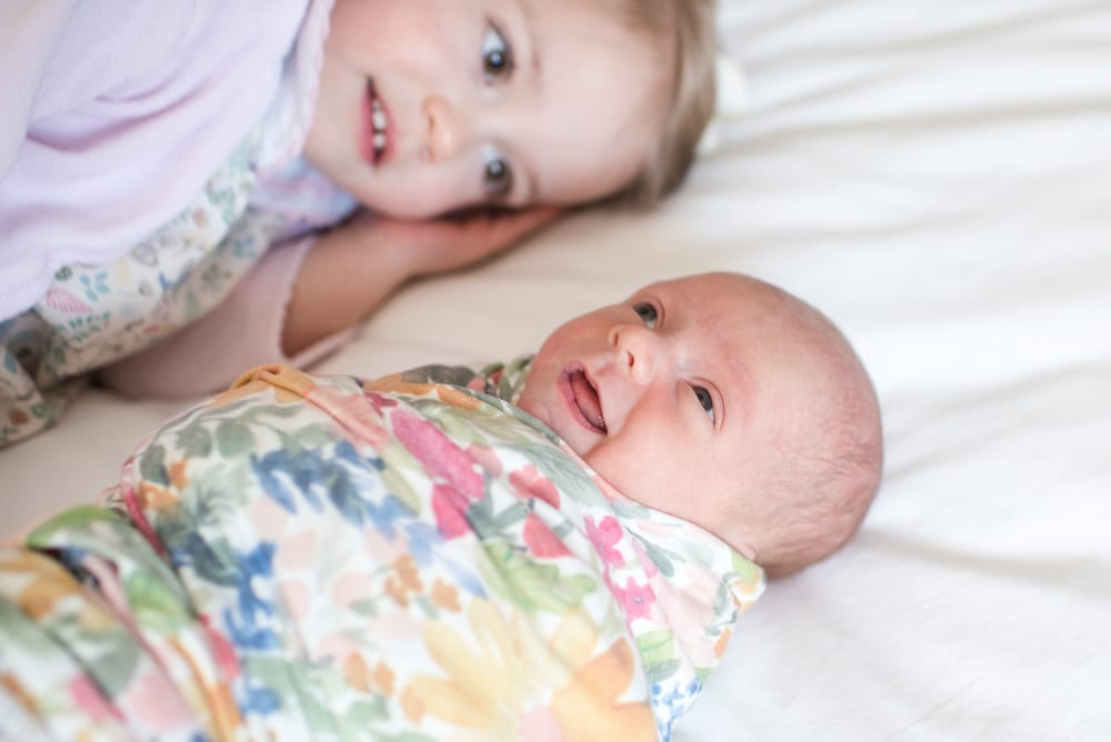 older sister lays with newborn baby girl