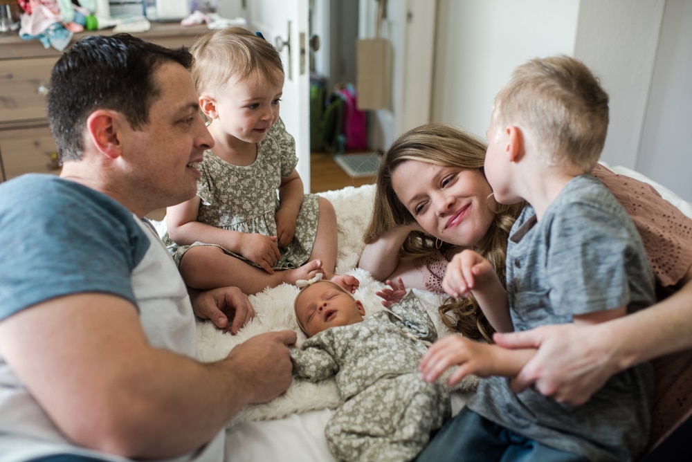 son kisses mom as his newborn baby sister lays on the bed