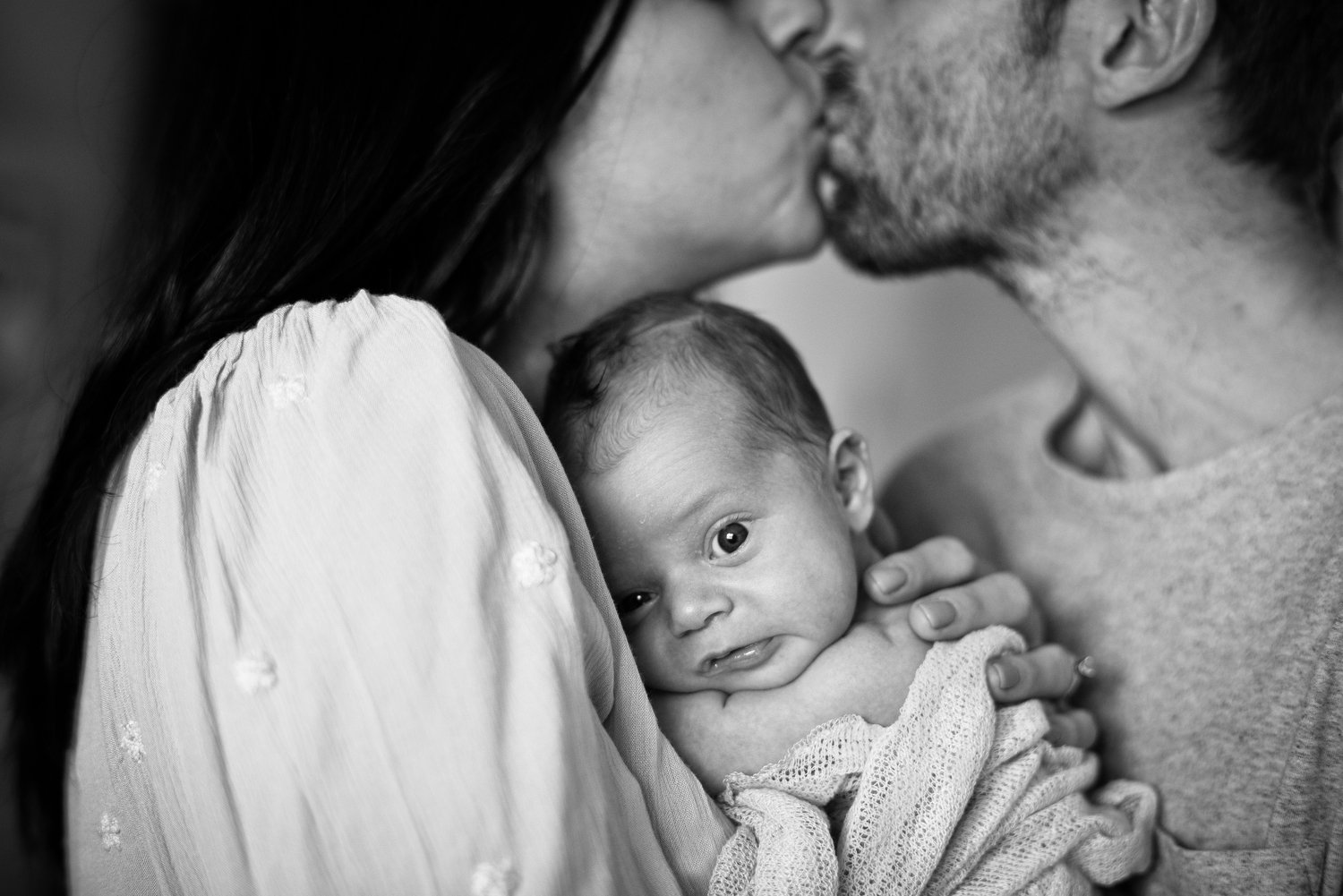 parents kiss as their baby snuggles close during Denver newborn portraits