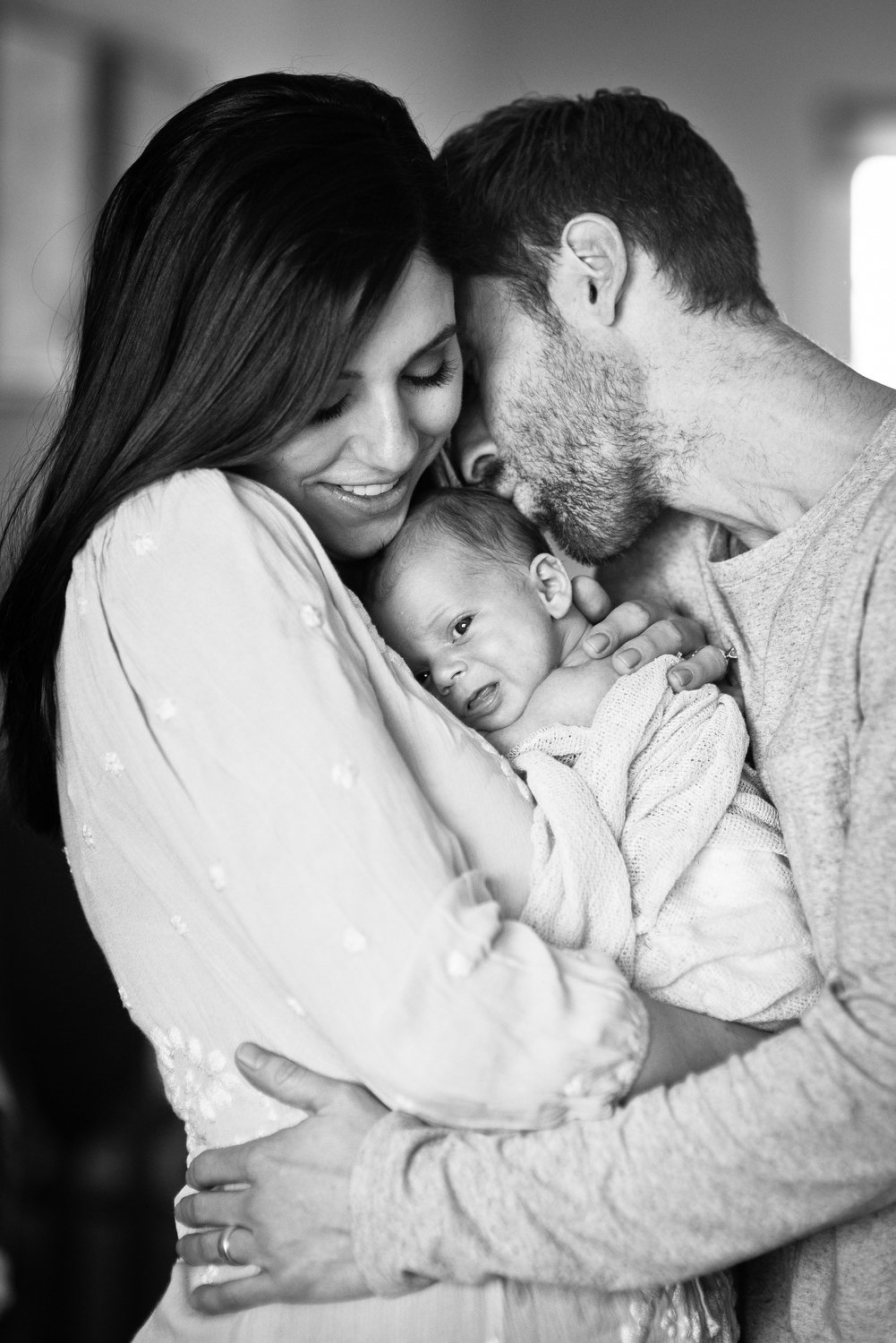 parents kiss their newborn baby as they do baby portraits in Denver