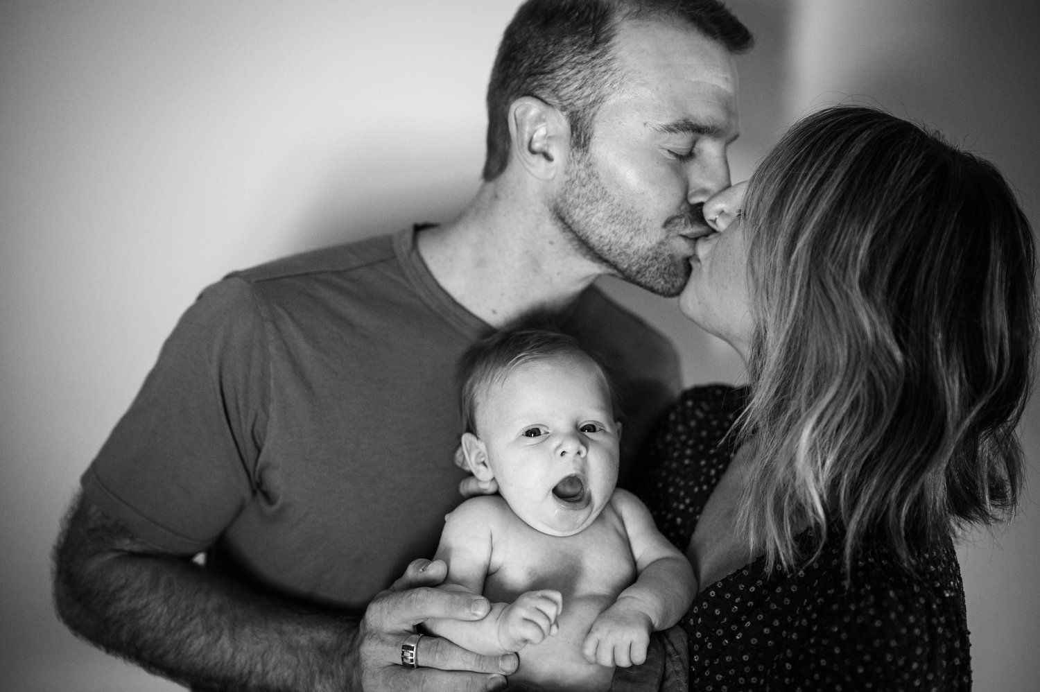 parents kiss while holding their newborn session