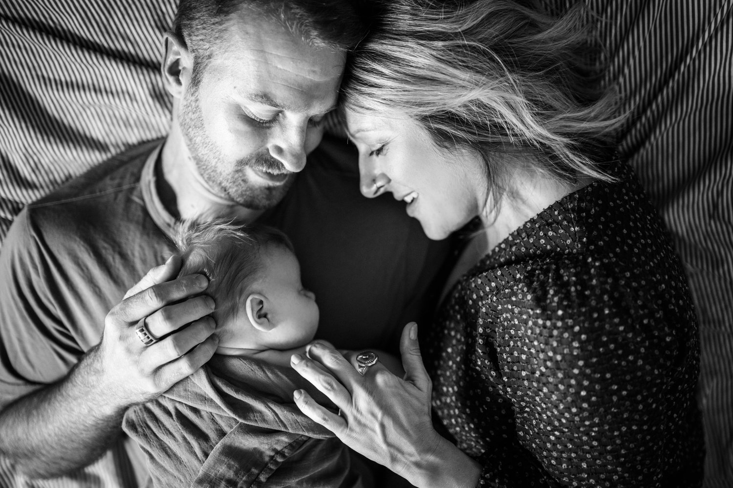 lifestyle newborn portraits of parents lying in bed with their newborn