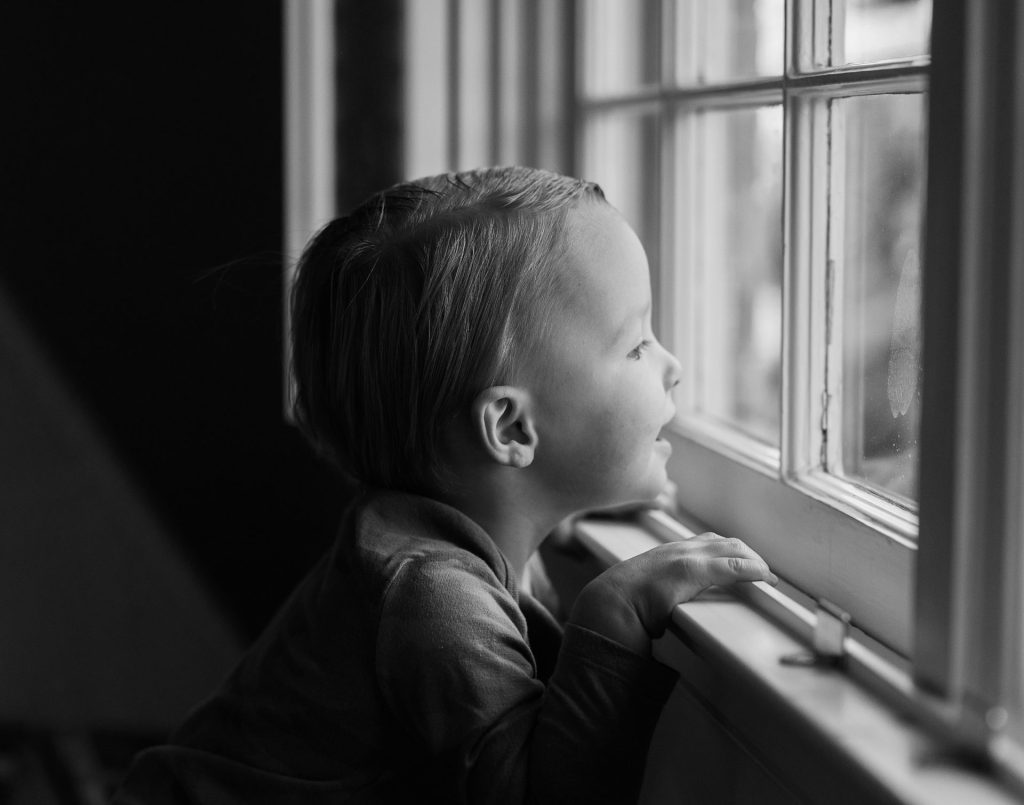 black and white photo of kid looking out the window