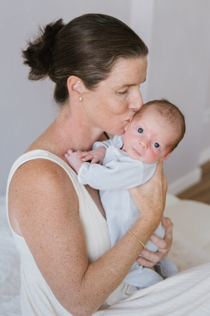 A new mom kisses her newborn son during their portraits at a Denver photo studio.