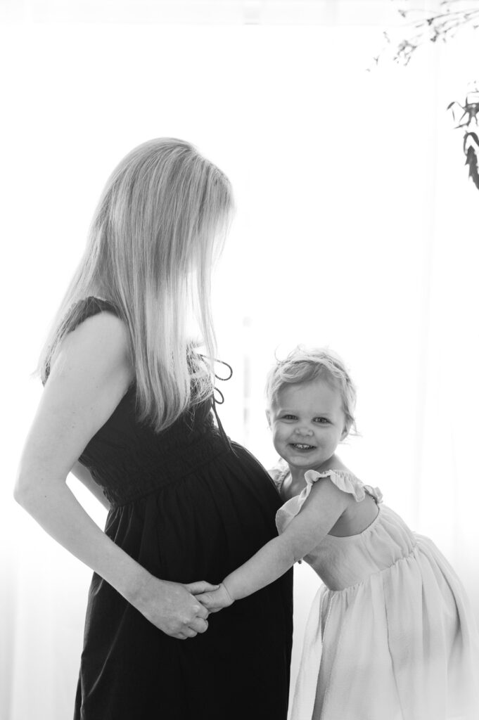 Daugher hugs her moms pregnant belly during maternity photos in Denver studio.