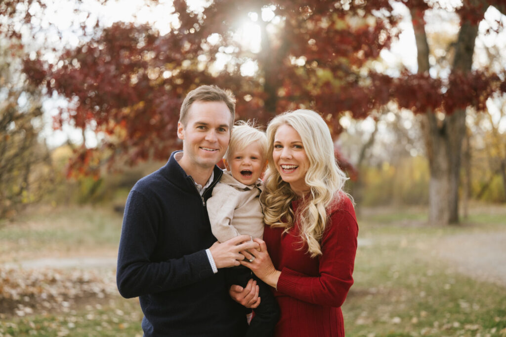A bright red tree is in the background during a family portrait.