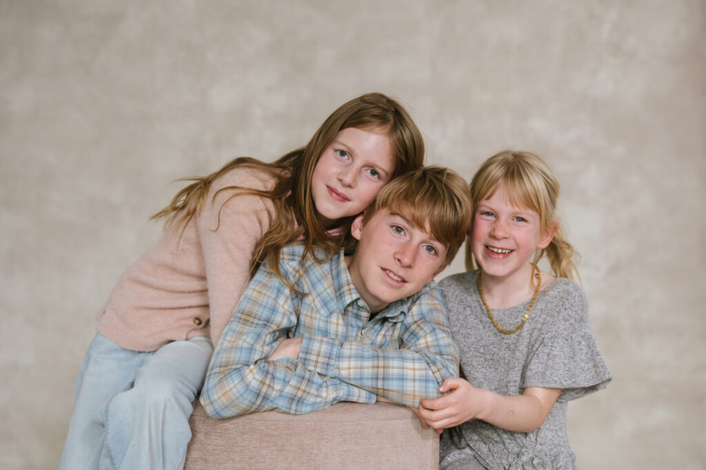 Three kids pose for a photo with a canvas backdrop in a photo studio in Denver.