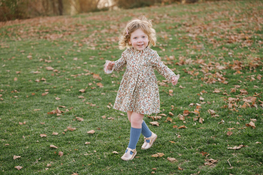 A little girl wearing knee socks runs in the leaves in Wash Park.