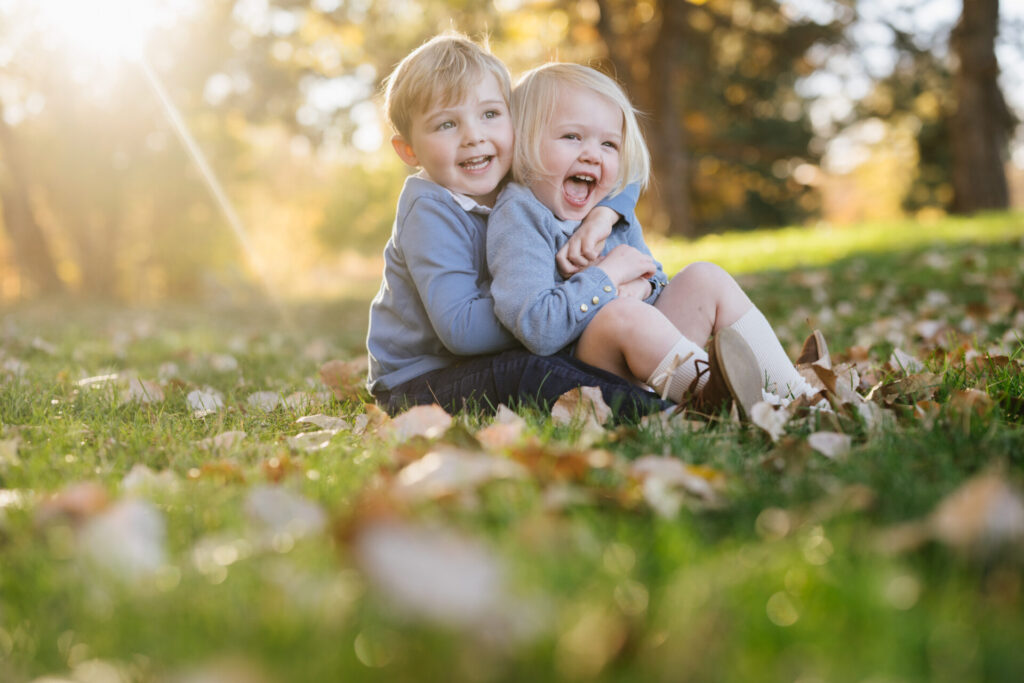 Siblings hug while sitting in the leaves in fall in Denver.